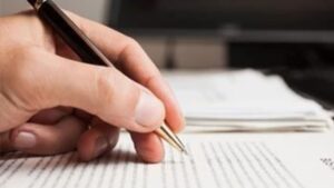 Hand signing legal document with pen on desk.